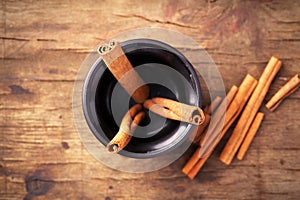 Cinnamon sticks in cup on old wooden background.