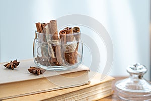Cinnamon sticks in glass jar, anise star, candles, vintage book on old rustic rustic wooden background.