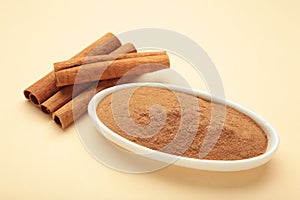 Cinnamon sticks and powder in bowl on beige background