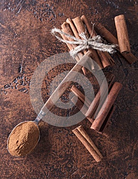 Cinnamon sticks and powder in spoon on a old copper table .