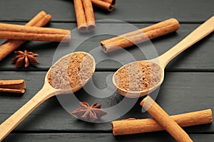 Cinnamon sticks and powder in wooden spoon on black wooden background
