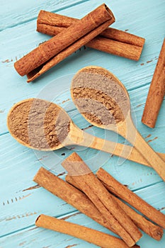 Cinnamon sticks and powder in wooden spoon on blue wooden background
