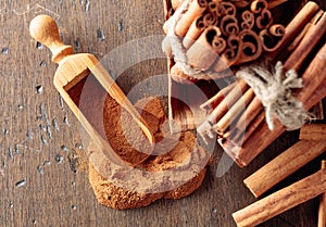 Cinnamon sticks and powder in a wooden spoon on an old wooden table