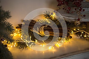 Cinnamon sticks tied with string in yellow lights garlands on Christmas tree branches and red berries. The atmosphere of the new y