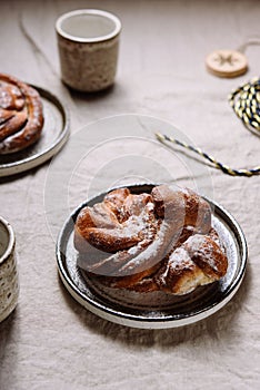 Cinnamon swirl brioche or Cinnamon roll bun and cups of cocoa on greige linen tablecloth