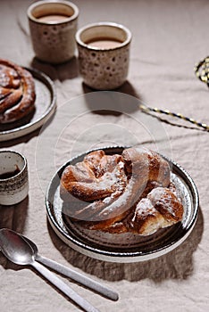 Cinnamon swirl brioche or Cinnamon roll bun and cups of cocoa on greige linen tablecloth