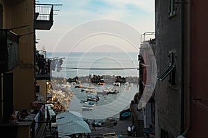 Cinque Terre, Italy - view of people in balconies, rocky harbor in Riomaggiore from a window. Boats docked in water. Fishing town