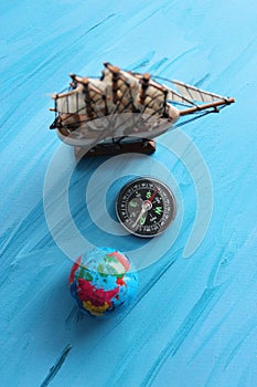 Circle Compass With Blurred Masted Ship Model And Small Globe Around On Blue Surface With Painted Waves