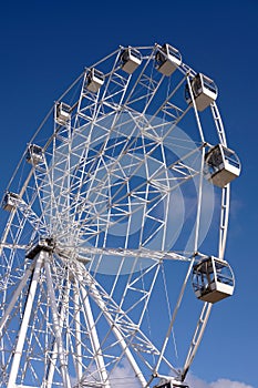 Circle ferris wheel from white metal construction with many rotating cabins over bright blue cloudless sky on sunny day