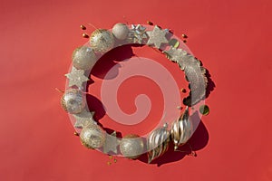 Circle frame wreath of gold christmas ornaments on a red background