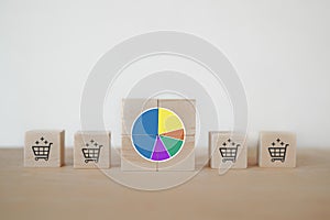 Circle graph showing market share portion on wooden cube blocks with blurred shopping cart symbol