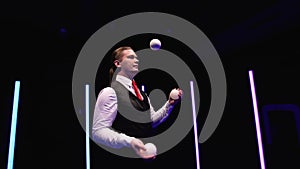 Circle movement camera around professional circus performer juggling white balls against a black studio background amid