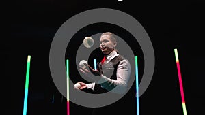 Circle movement camera around professional circus performer juggling white balls against a black studio background amid