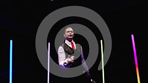 Circle movement camera around professional circus performer spinning pins against a black studio background amid bright