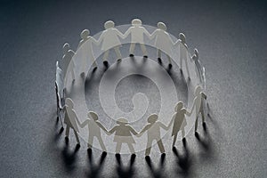 Circle of paper people holding hands on dark surface. Community, union concept. Society and support.