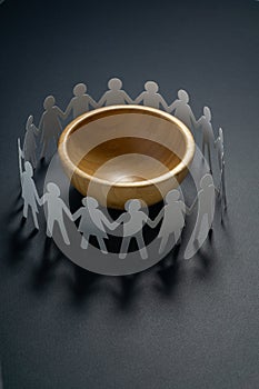 Circle of paper people holding hands in front of big empty bowl. Overpopulation, famine concept.