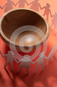 Circle of paper people holding hands in front of big empty bowl. Overpopulation, famine concept.