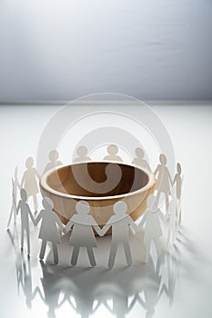 Circle of paper people holding hands in front of big empty bowl. Overpopulation, famine concept.