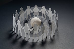 Circle of paper people holding hands in front of white ball. Brotherhood, cult concept. photo