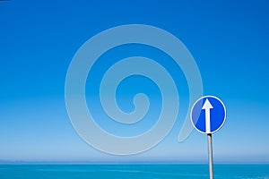 Circle road sign with white arrow on blue sky background.