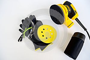 Circular electric power sander,disconnected container for dust.Work gloves,protection goggles,sandpaper disc on white
