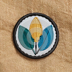 A circular embroidered patch with three stylized leaf shapes beige fabric background photo