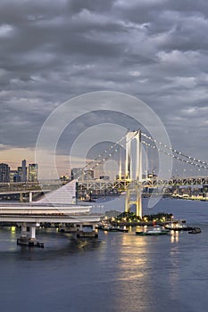 Circular highway leading to the Rainbow Bridge with Cargo and cruise ships moored or sailing in Odaiba Bay of Tokyo