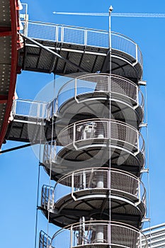 Circular iron staircase for fire escape outside a modern metal industrial building fence in the open air