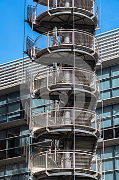 Circular iron staircase for fire escape outside a modern metal industrial building fence in the open air