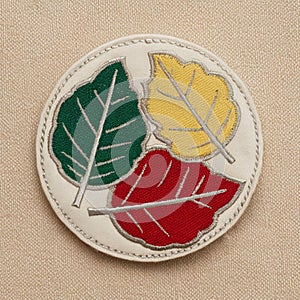 A circular patch with three overlapping leaf sewn onto a neutral cream fabric surface photo