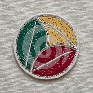 A circular patch with three overlapping leaf sewn onto a neutral cream fabric surface photo