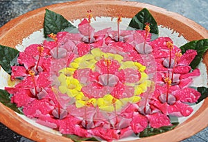 A circular pattern of red and yellow flowers floating in a terracotta bowl.
