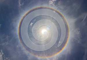 Circular rainbow halo around the sun among blue sky and white clouds