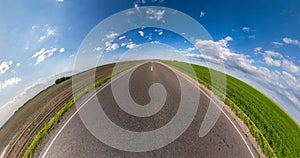 Circular rotation of the hemisphere of the earth on asphalt road among green field in blue sky.
