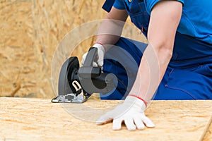 Circular saw in the hands of a man sawing a wooden plank, close-up