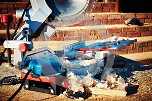 Circular saw stands in sawdust strewn after sawing wooden carved platbands