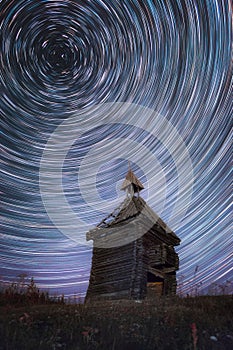 Circular Star Trails in night sky above old abandoned wooden chapel