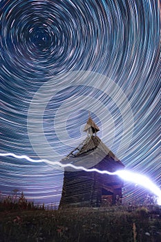 Circular Star Trails in night sky above old abandoned wooden chapel