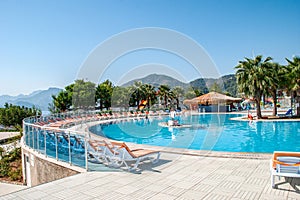 Circular swimming pool surrounded by lounge chairs and a bar with a thatched roof in water park