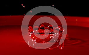 Circular water splash forming a crown-shaped figure taken in macro mode in a red container with a black upper background