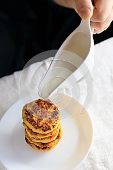 A circumcised man in a black T-shirt holds a white gravy boat in his hands and pours the curd cheesecakes on a plain