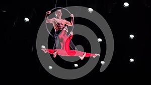 Circus aerial hoop duo on black background performing risky tricks. Man and women fly on stage