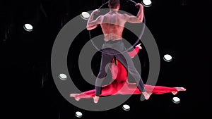 Circus aerial hoop duo on black background performing risky tricks. Man and women fly on stage