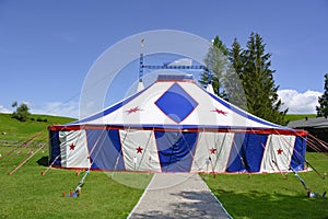 Circus tent, small circus tent in blue and white with red stars standing on green meadow.
