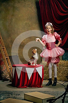 Circus trainer. Portrait of little cute beautiful girl in festive dress training funny doggy at vintage circus. Holidays