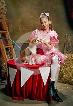 Circus trainer. Portrait of little cute beautiful girl in festive dress training funny doggy at vintage circus. Holidays