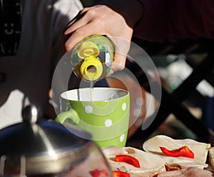 A citron juice addicting to green, spotted cup for snack. Also there is bread with ham and red pepper. Snack after work