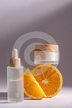 Citrus cosmetics with Vitamin C and orange slices on gray background. Face serum in dropper bottle and cream jar. Blank