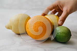 Citrus or fruit mix of orange, lemon and lime on the table. A woman`s hand takes a lemon