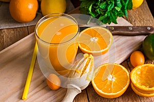 Citrus fruits oranges lemons lime cumquat, fresh mint, reamer, freshly pressed juice in glass on table photo